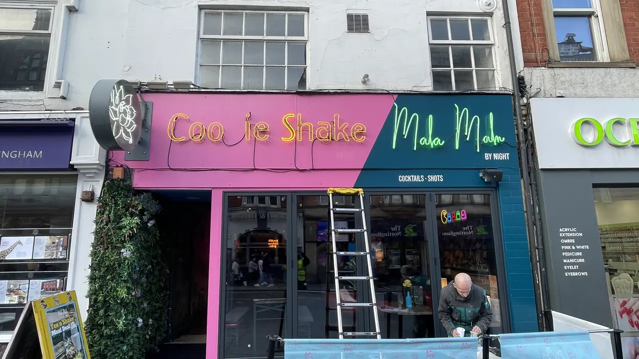 Installer fitting a colourful shop front sign from a ladder